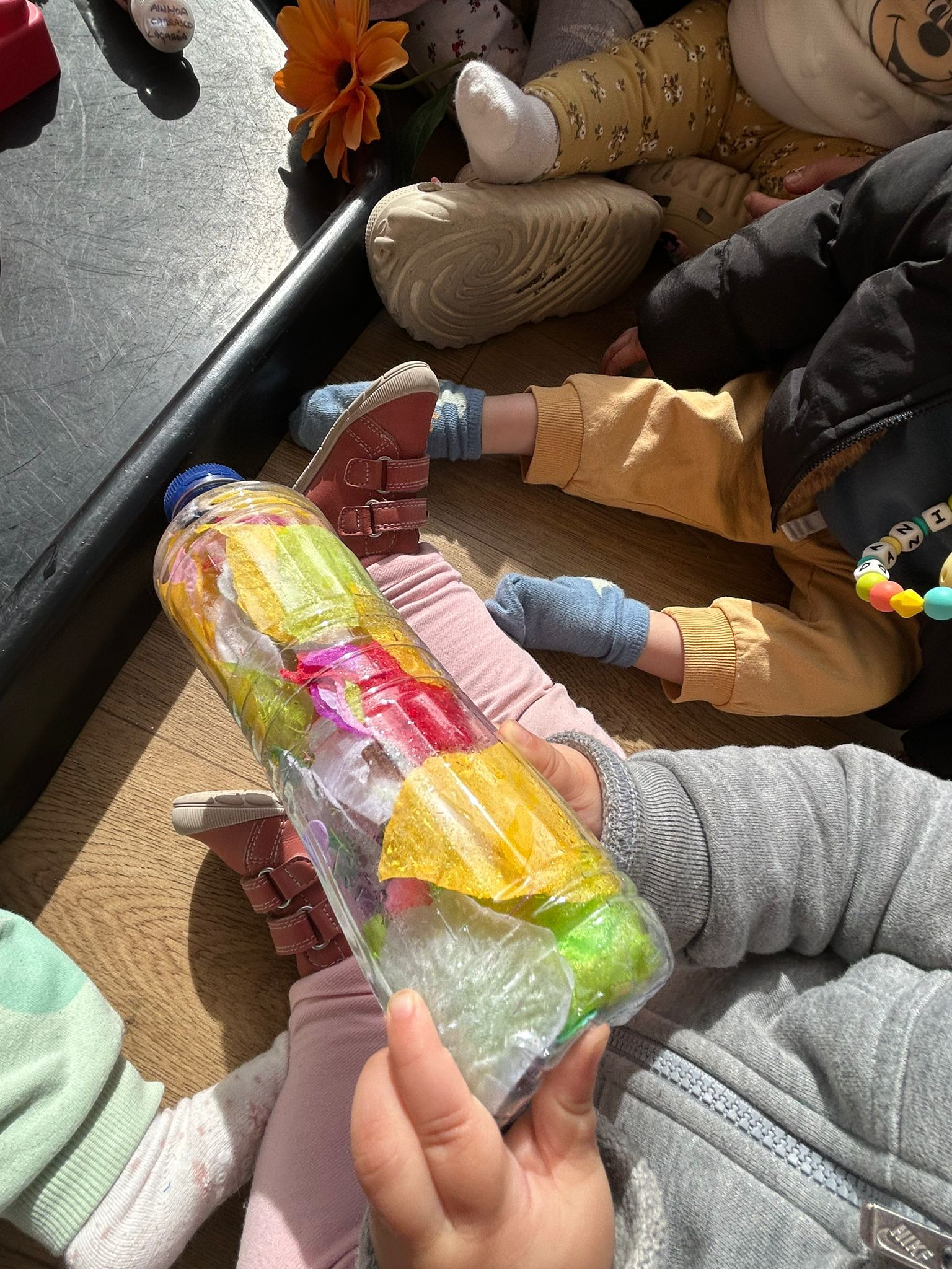 Un bebé en la escuela infantil El Columpio sosteniendo una botella sensorial rellena de papeles de colores vibrantes.