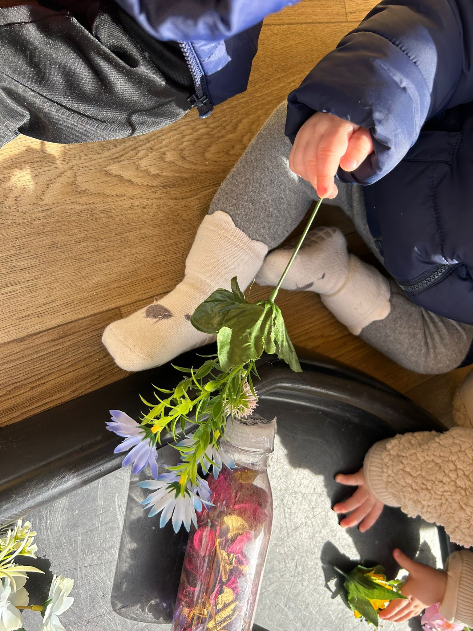 Detalle de la mano de un bebé manipulando flores y piezas de colores en la Escuela Infantil El Columpio.