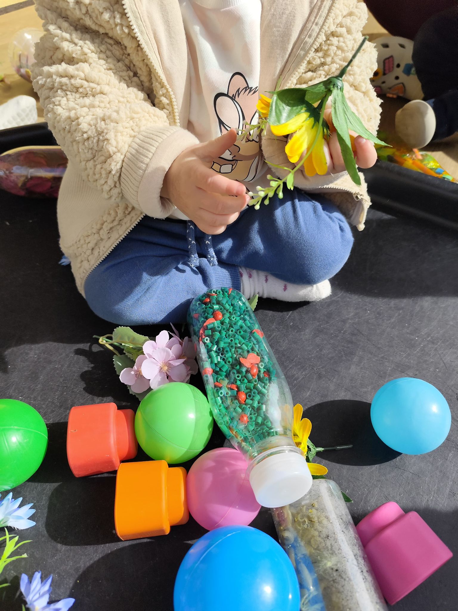 Plano detalle de un bebé en la escuela infantil El Columpio oliendo y tocando flores artificiales blancas y amarillas.